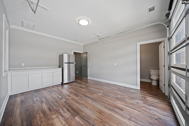 unfurnished bedroom featuring crown molding, freestanding refrigerator, wood finished floors, and visible vents