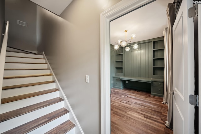 stairs featuring a notable chandelier, visible vents, and wood finished floors
