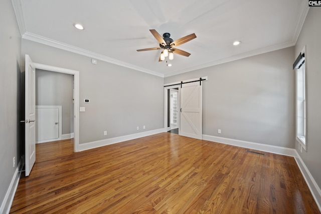 unfurnished bedroom featuring crown molding, baseboards, a barn door, and wood finished floors
