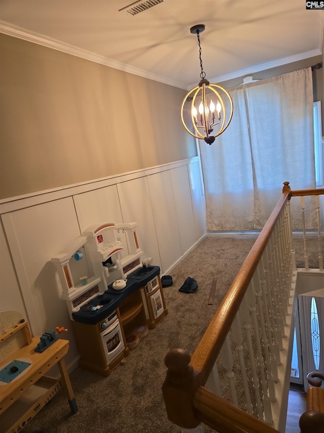 interior space featuring visible vents, crown molding, a chandelier, carpet, and a decorative wall