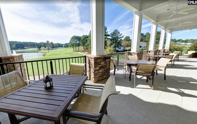 view of patio with a water view, view of golf course, a ceiling fan, and outdoor dining space