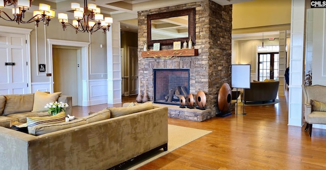 living area with an inviting chandelier, beam ceiling, a stone fireplace, wood finished floors, and coffered ceiling