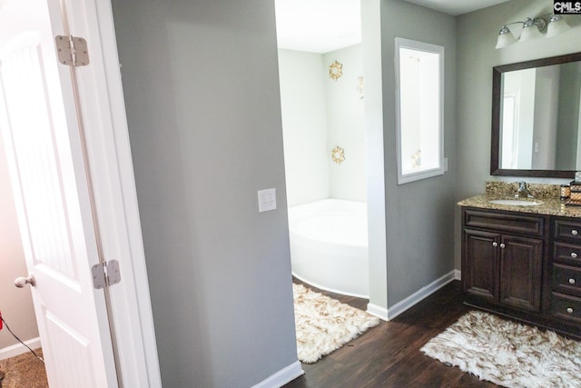 full bath with baseboards, vanity, a garden tub, and wood finished floors