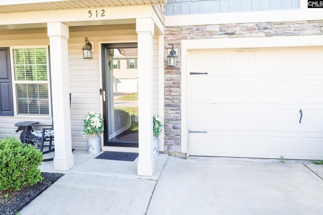 entrance to property featuring a porch, a garage, driveway, and stone siding