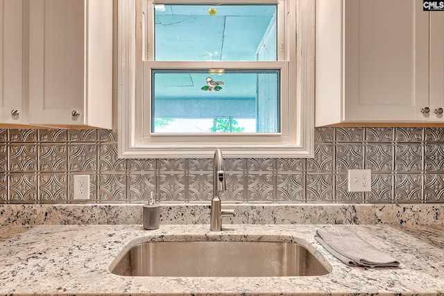 interior details with white cabinets, backsplash, light stone countertops, and a sink