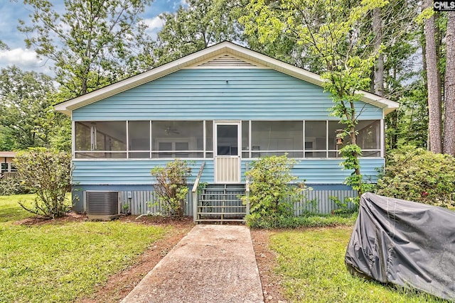 bungalow-style home featuring a sunroom, a front lawn, and cooling unit