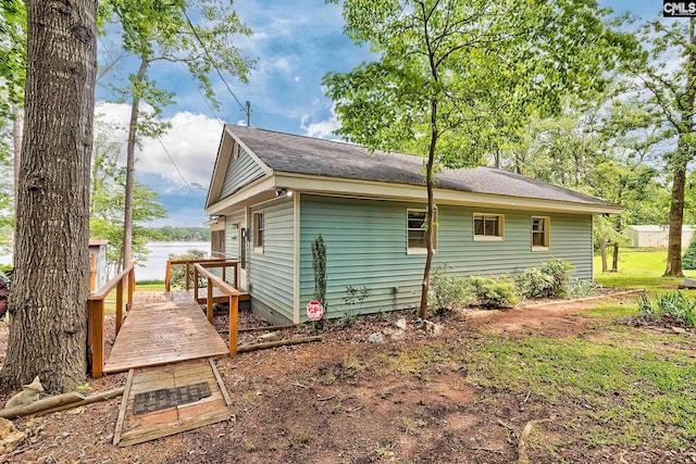 view of side of home with crawl space, a deck with water view, and roof with shingles