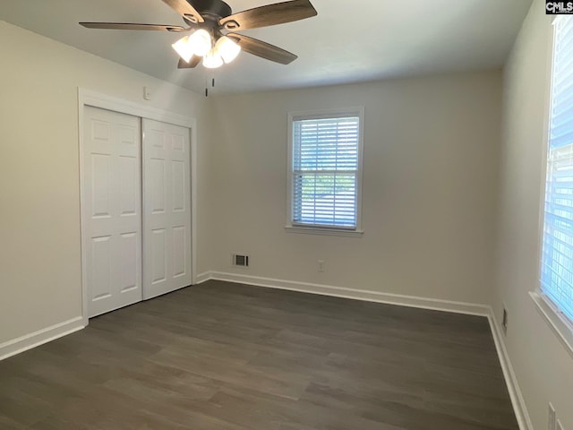 unfurnished bedroom featuring baseboards, dark wood-style floors, multiple windows, and a closet