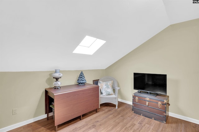 sitting room with vaulted ceiling with skylight, baseboards, and wood finished floors