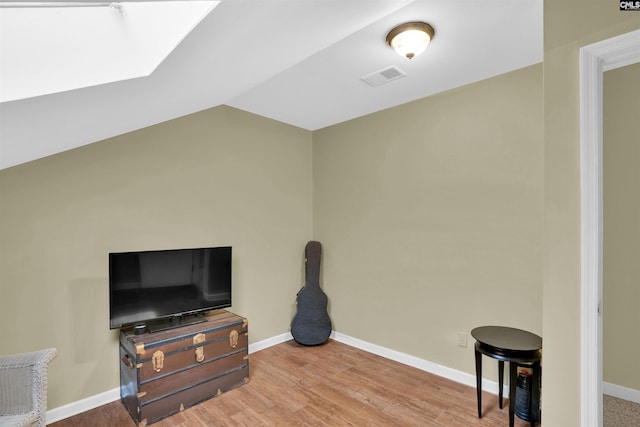 interior space with visible vents, baseboards, lofted ceiling with skylight, and wood finished floors