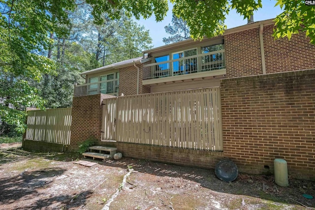 back of house featuring brick siding and a balcony
