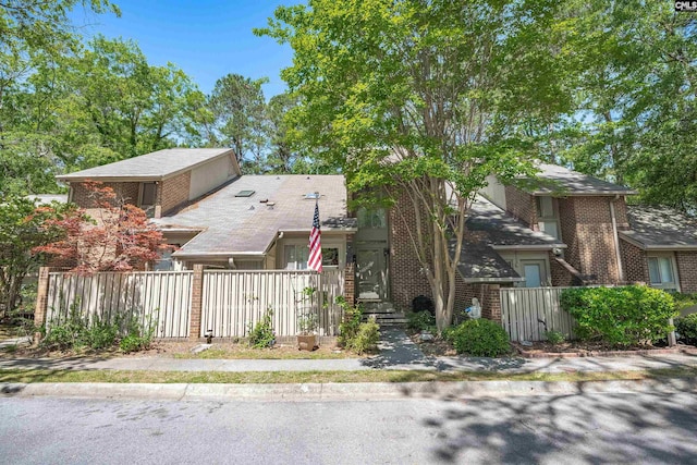 view of front of house featuring fence private yard, a shingled roof, and brick siding