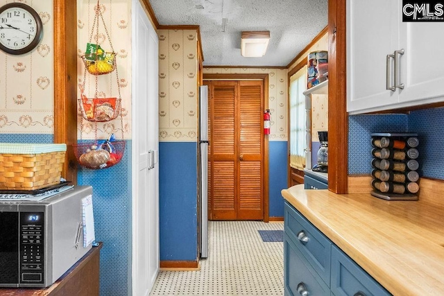 interior space with light countertops, blue cabinetry, stainless steel microwave, wallpapered walls, and light floors
