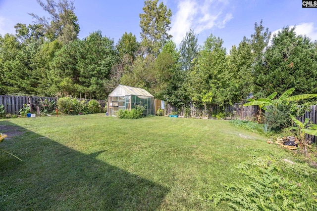 view of yard featuring a greenhouse, an outbuilding, and a fenced backyard