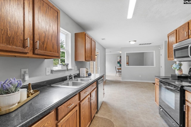 kitchen featuring dark countertops, a sink, brown cabinetry, stainless steel appliances, and visible vents