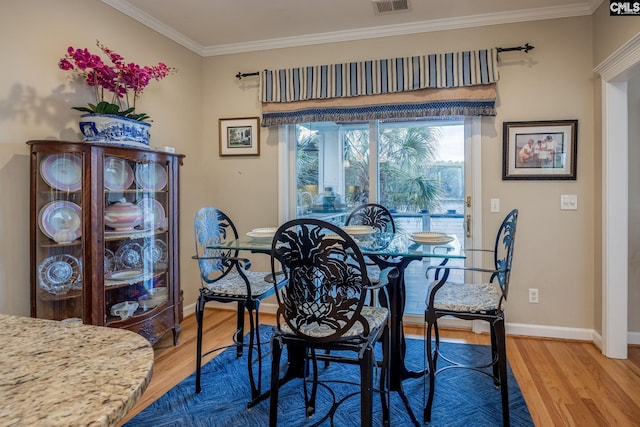 dining area featuring baseboards, ornamental molding, light wood-type flooring, and visible vents
