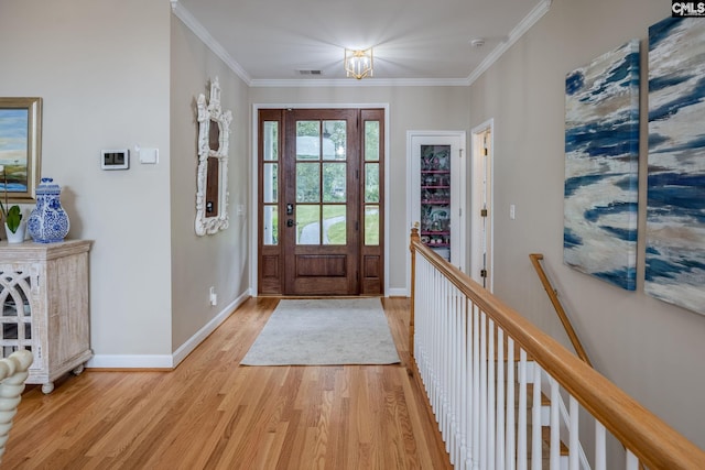 foyer entrance featuring light wood-style floors, ornamental molding, baseboards, and visible vents