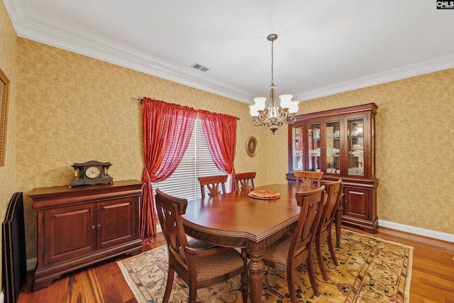 dining area with an inviting chandelier, crown molding, visible vents, wood finished floors, and wallpapered walls