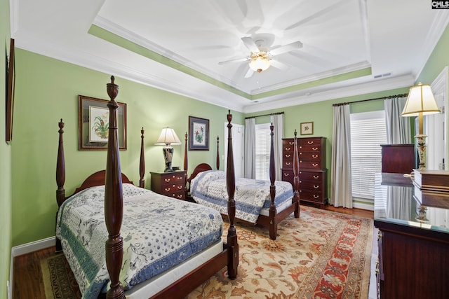 bedroom featuring ceiling fan, wood finished floors, a tray ceiling, visible vents, and ornamental molding