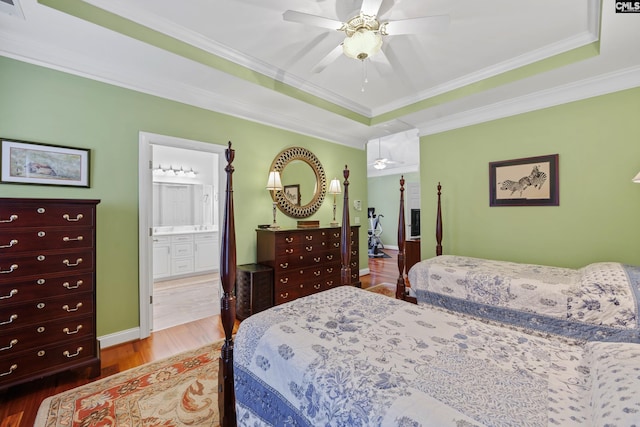 bedroom featuring crown molding, a tray ceiling, wood finished floors, and ensuite bathroom