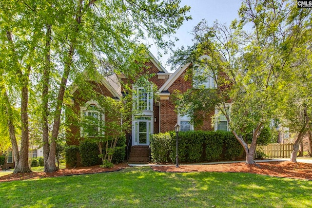 traditional-style house featuring fence, a front lawn, and brick siding