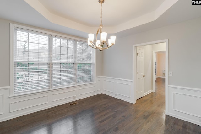 unfurnished dining area featuring a raised ceiling, plenty of natural light, a wainscoted wall, and a chandelier