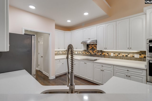 kitchen with freestanding refrigerator, dark wood-style floors, black electric cooktop, under cabinet range hood, and tasteful backsplash