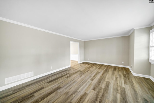 empty room featuring baseboards, ornamental molding, wood finished floors, and visible vents