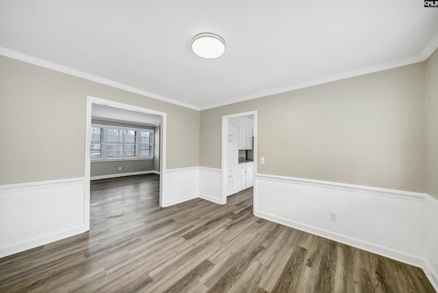 spare room featuring ornamental molding, wood finished floors, and a wainscoted wall