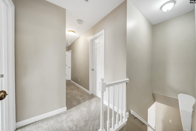 hall featuring baseboards, attic access, carpet, and an upstairs landing