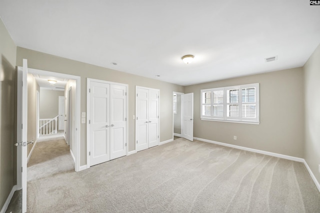 unfurnished bedroom with two closets, baseboards, visible vents, and light carpet
