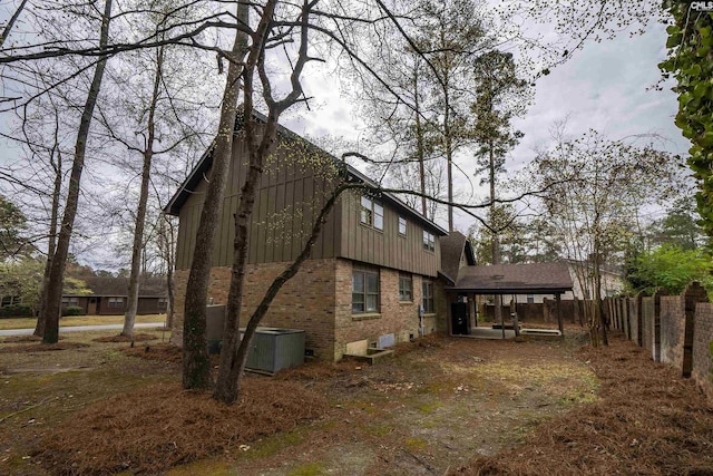view of home's exterior featuring board and batten siding, brick siding, central AC, and fence