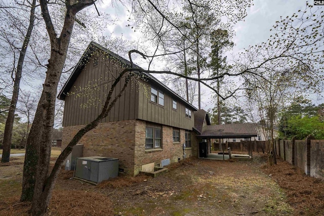 rear view of house with fence, brick siding, board and batten siding, cooling unit, and a detached carport