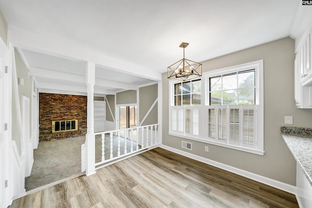 unfurnished dining area featuring visible vents, a fireplace, baseboards, a notable chandelier, and light wood-style floors