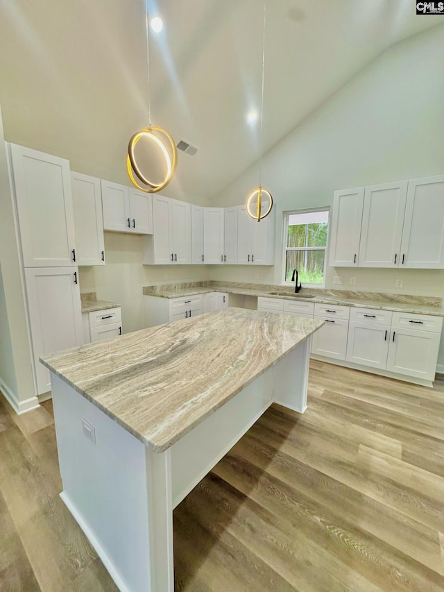 kitchen featuring visible vents, a kitchen island, light stone countertops, high vaulted ceiling, and white cabinets