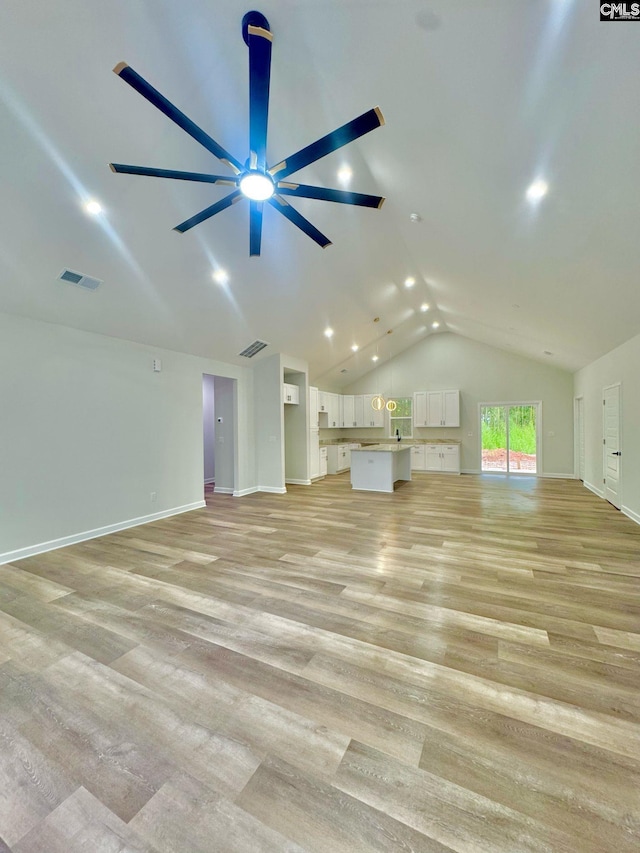 unfurnished living room featuring a ceiling fan, visible vents, vaulted ceiling, and light wood-style floors