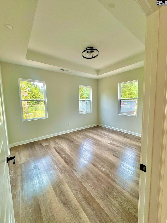 empty room with a tray ceiling, visible vents, baseboards, and light wood-style floors