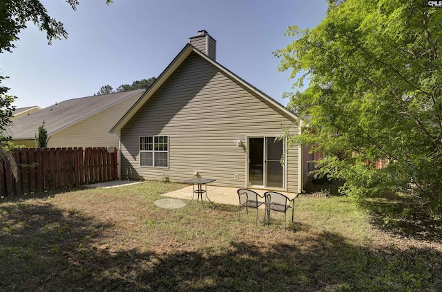back of house featuring a yard, a patio, fence, and a chimney