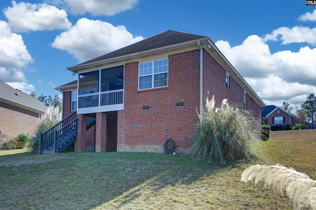 back of property with a lawn, ceiling fan, stairway, and brick siding