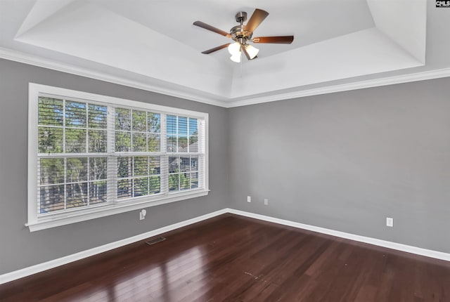 spare room with baseboards, a tray ceiling, wood finished floors, and visible vents