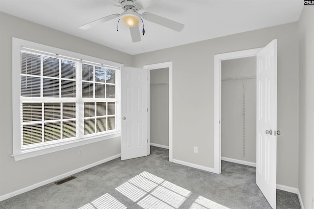 unfurnished bedroom featuring carpet floors, multiple closets, a ceiling fan, baseboards, and visible vents