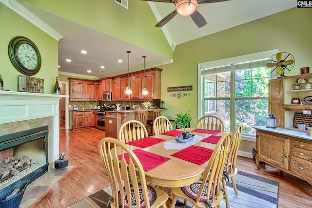dining space featuring crown molding, ceiling fan, a fireplace, light wood-style flooring, and visible vents