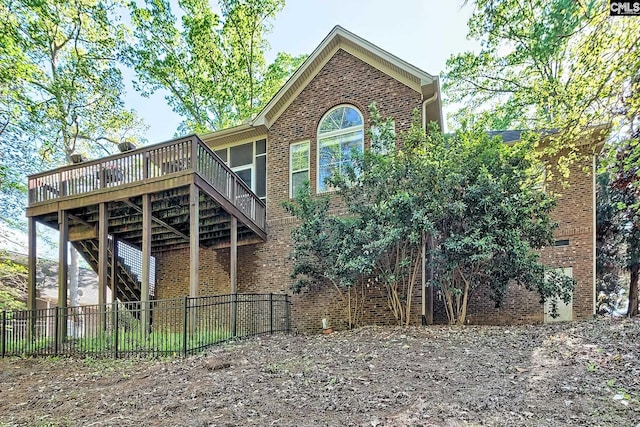 back of property with brick siding, a wooden deck, fence private yard, and stairway