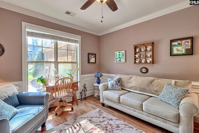 living room with ceiling fan, wainscoting, wood finished floors, visible vents, and ornamental molding
