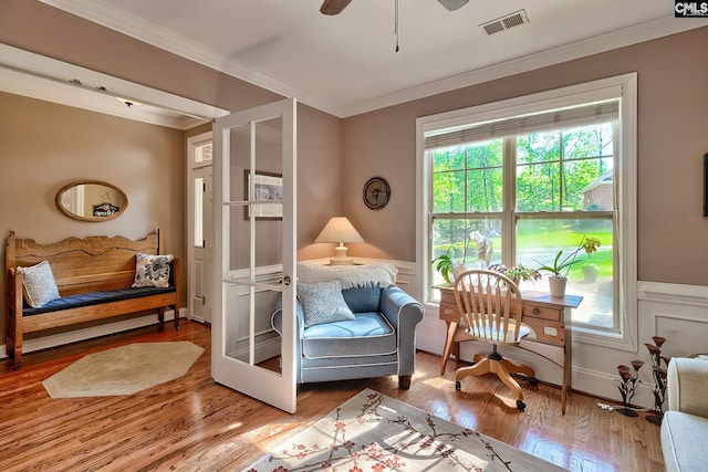 sitting room featuring visible vents, ornamental molding, wood finished floors, and a wainscoted wall