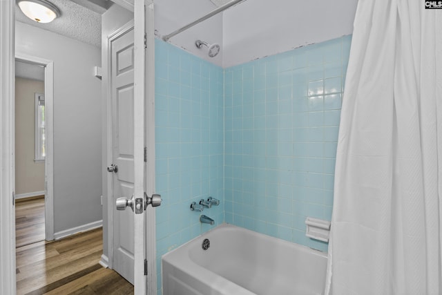 bathroom featuring a textured ceiling, baseboards, shower / bath combo, and wood finished floors