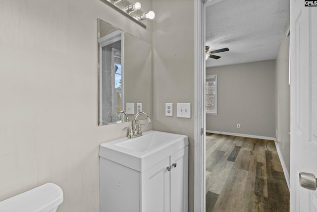 half bath with ceiling fan, vanity, toilet, a textured ceiling, and wood finished floors