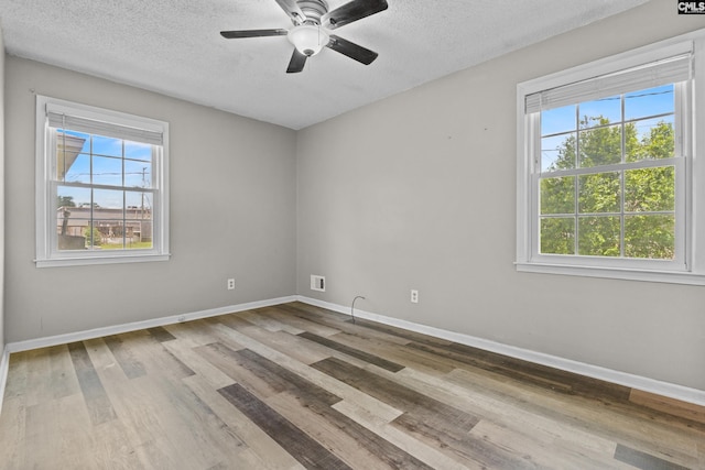 unfurnished room with a textured ceiling, baseboards, a healthy amount of sunlight, and wood finished floors