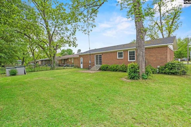 rear view of property featuring brick siding, fence, a yard, and entry steps