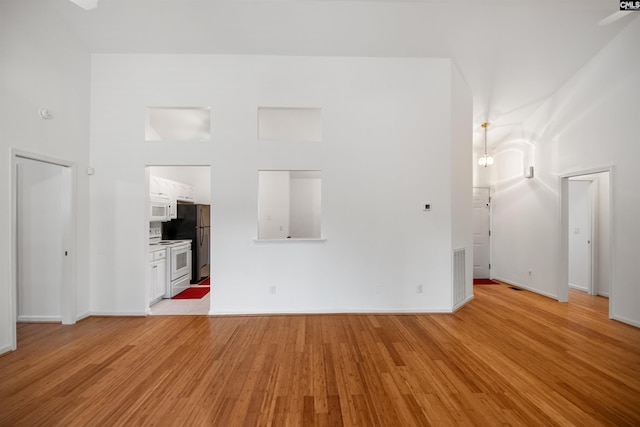 unfurnished living room with baseboards, visible vents, light wood finished floors, and a towering ceiling